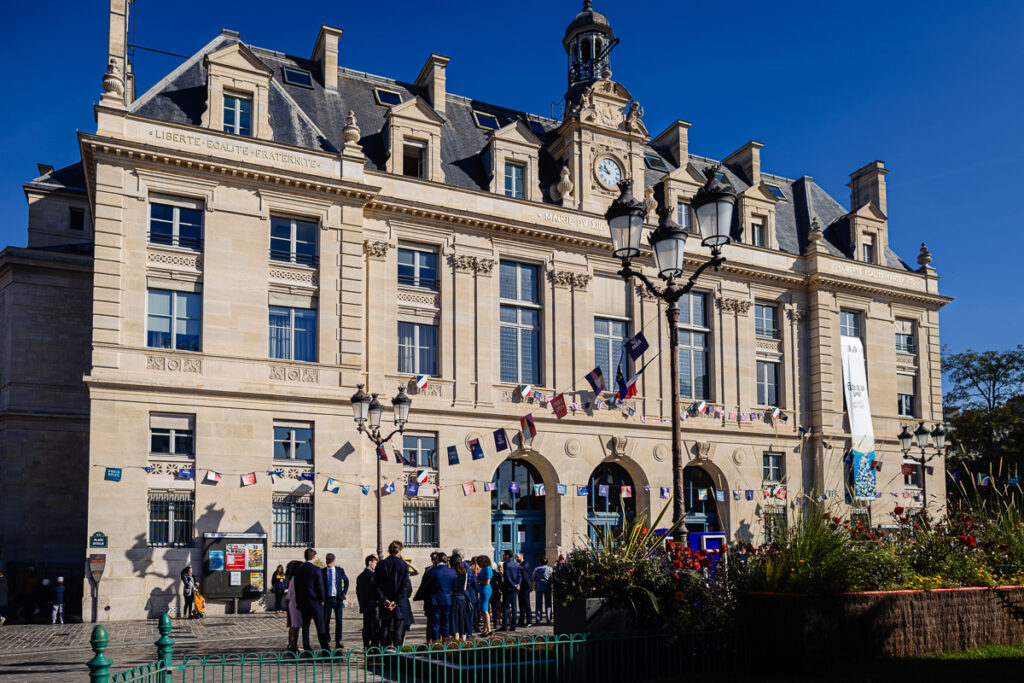 Les gens se rassemblent devant un bâtiment historique en pierre orné de drapeaux et d'une tour d'horloge.