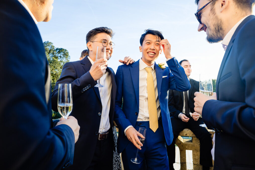 Groupe de personnes en tenue de soirée souriant et tenant des coupes de champagne à l'extérieur pendant la journée.