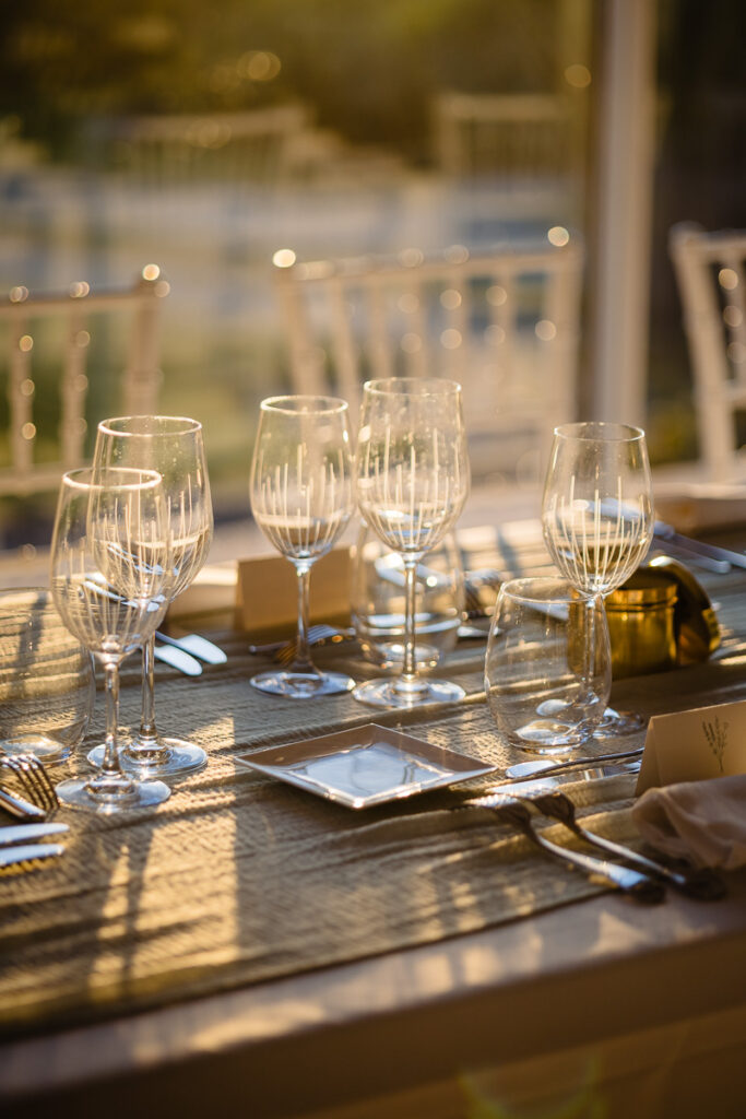 Décoration de table élégante avec plusieurs verres à vin, assiettes et couverts sur une table ensoleillée ornée d'un tapis tissé.