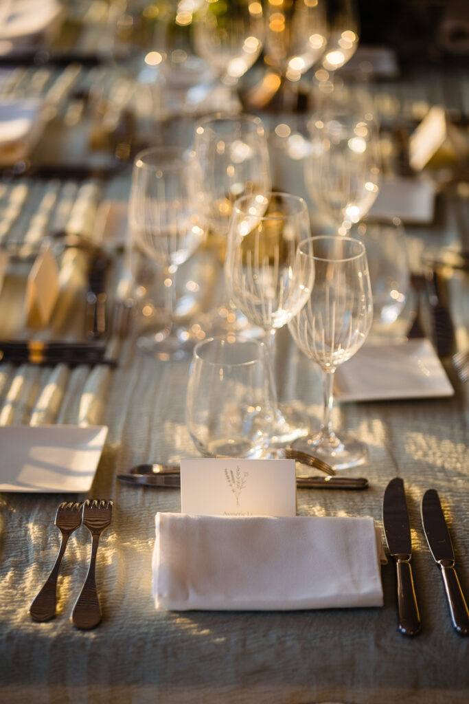 Décoration de table élégante avec verres à vin, serviettes, couverts et marque-place, le tout soigneusement disposé sur une nappe à motifs.