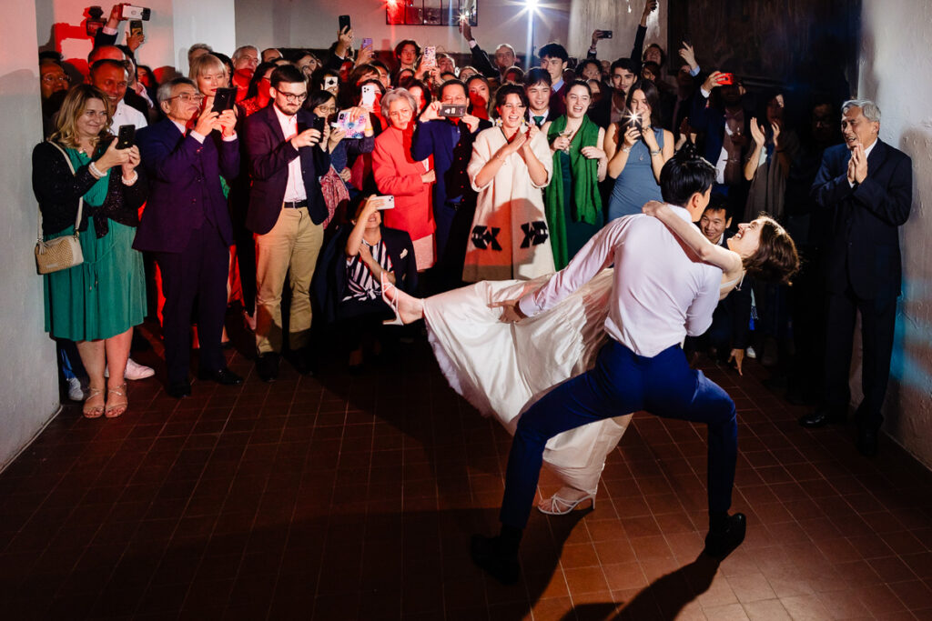 Un couple exécute un plongeon de danse devant une foule rassemblée lors d'un événement en salle, les participants capturant le moment sur leurs téléphones.